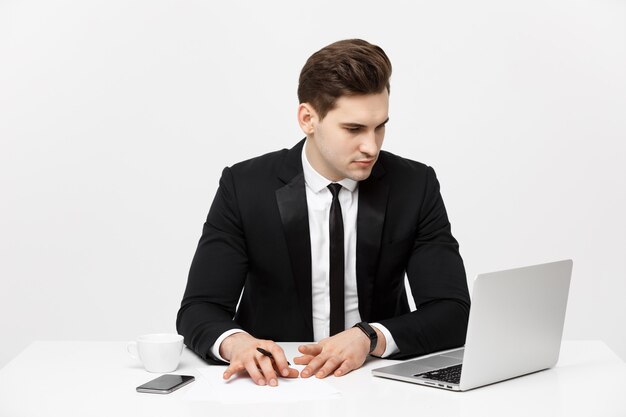 Retrato de um empresário bonito segurando um smartphone enquanto trabalha em um computador em sua mesa, ele é ...