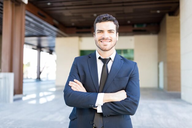 Retrato de um empresário hispânico de boa aparência, braços cruzados do lado de fora do escritório