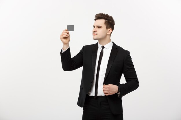 Retrato de um empresário segurando um cartão de crédito e verificando seriamente isolado sobre fundo cinza.