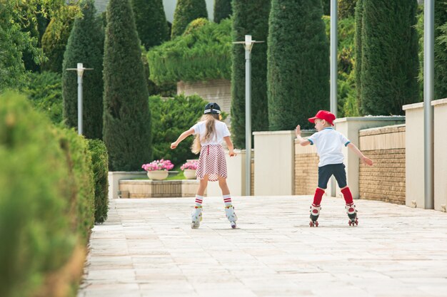 Retrato de um encantador casal adolescente patinando juntos de patins no parque. Menino e menina adolescentes caucasianos