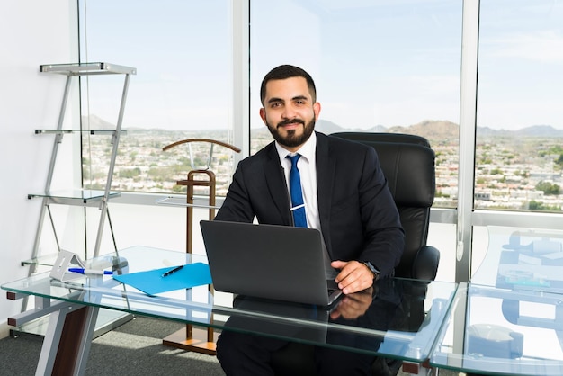 Retrato de um executivo de negócios bonito e empresário se sentindo feliz e fazendo um trabalho lucrativo em seu escritório elegante com vista para a cidade grande