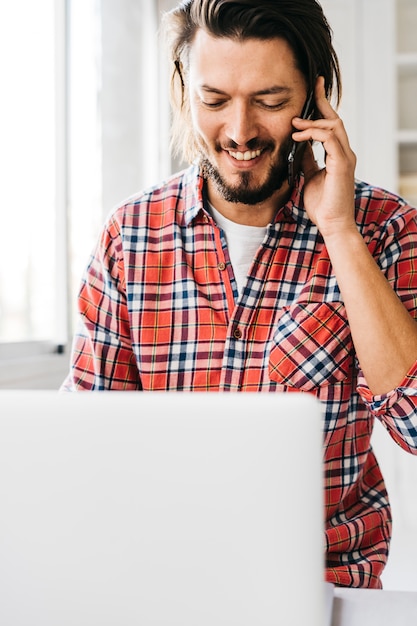 Retrato, de, um, feliz, homem jovem, falando telefone móvel, olhar, laptop