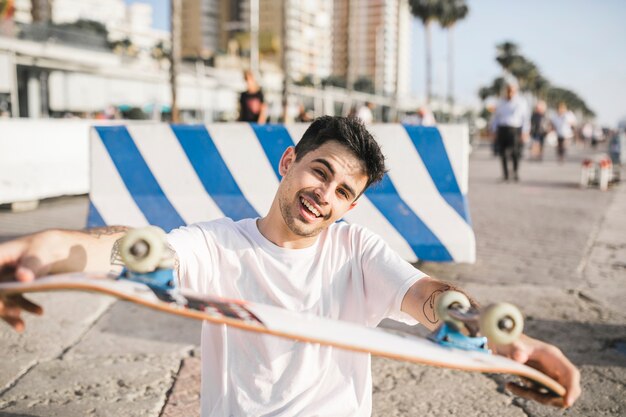 Retrato, de, um, feliz, homem jovem, mostrando, seu, skateboard