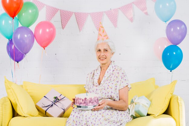 Retrato, de, um, feliz, mulher sênior, sentar sofá, com, bolo aniversário