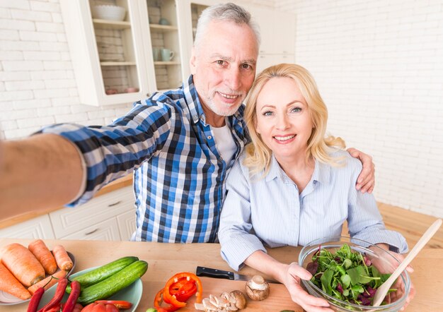 Retrato, de, um, feliz, par velho, levando, selfie, enquanto, preparar, salada, cozinha