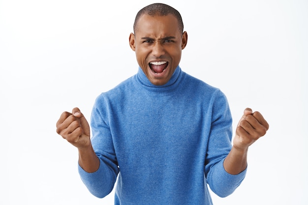 Retrato de um homem afro-americano forte e entusiasmado, gritando, aumentando a confiança, assistindo à transmissão ao vivo de um jogo de esporte na tv online