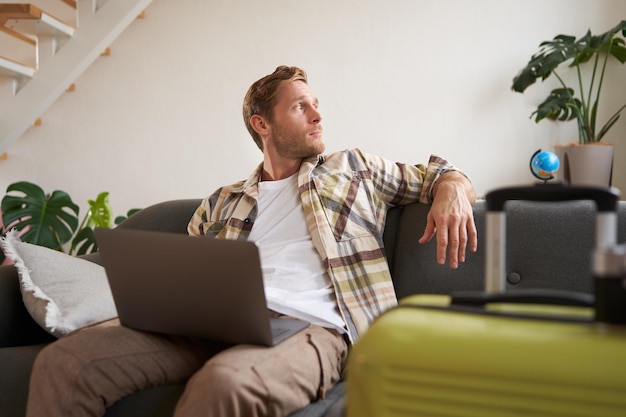 Foto grátis retrato de um homem alegre indo de férias planeja uma viagem de viagem no exterior tem laptop aberto senta-se em