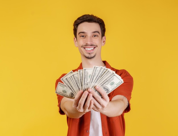 Retrato de um homem alegre segurando notas de dólar sobre fundo amarelo