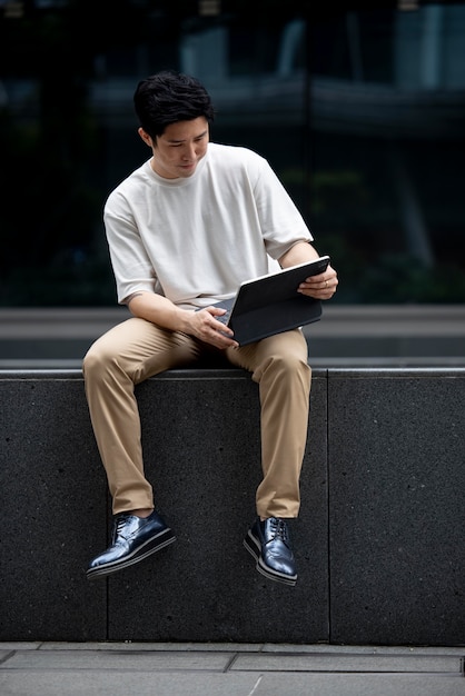 Retrato de um homem asiático bonito usando laptop ao ar livre na cidade