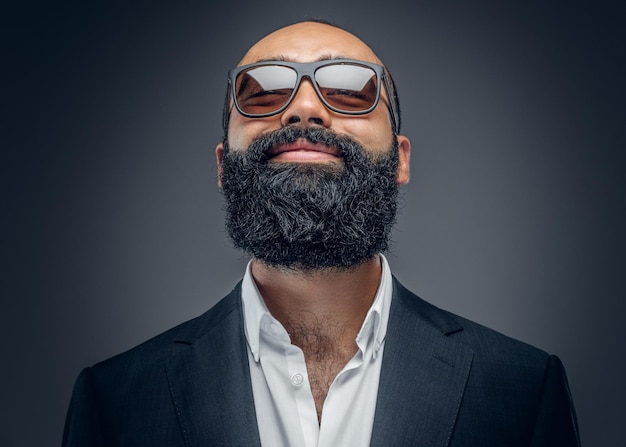 Foto grátis retrato de um homem barbudo elegante de terno e óculos de sol isolados em fundo cinza.