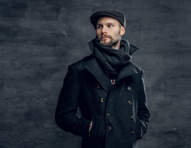 Retrato de um homem barbudo hipster vestido com uma jaqueta cinza e um gorro de lã isolado em fundo cinza.