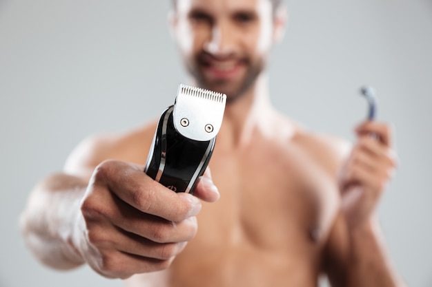 Retrato de um homem barbudo sorridente feliz mostrando barbeador elétrico