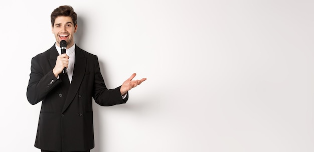 Foto grátis retrato de um homem bonito de terno preto cantando uma música segurando o microfone e dando discurso em pé