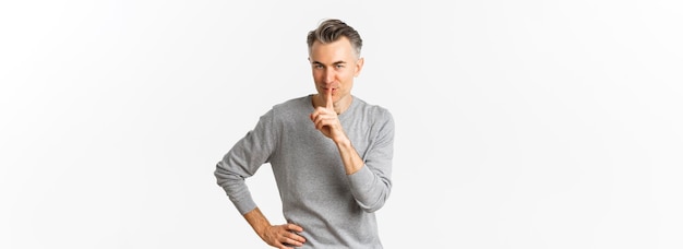 Retrato de um homem bonito e astuto com cabelos grisalhos, silenciando e sorrindo, contando o segredo, prepare a surpresa