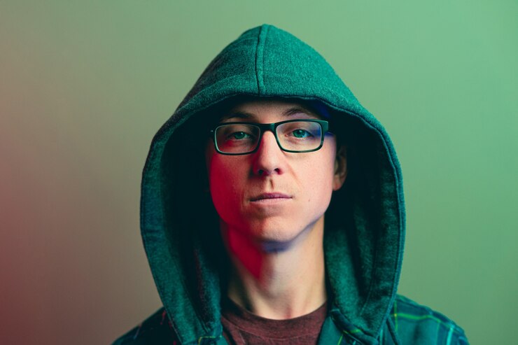 Foto grátis retrato de um homem branco com uma cara de pau, usando óculos e um casaco com capuz com efeito de luz verde