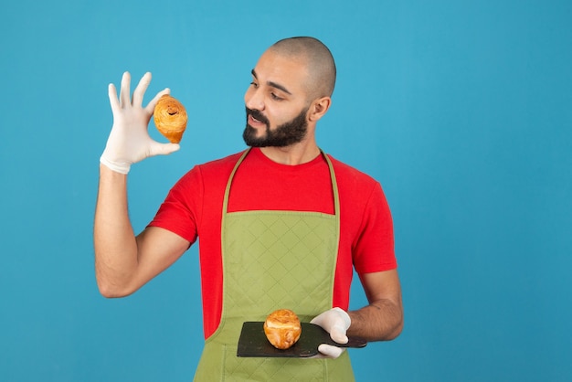 Retrato de um homem de avental e luvas segurando bolos frescos.