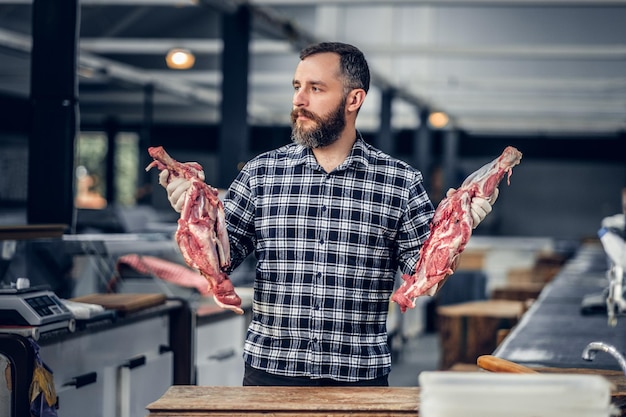 Retrato de um homem de carne barbudo vestido com uma camisa de lã segura carne fresca cortada em um mercado.