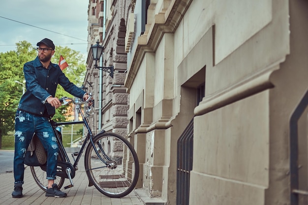 Retrato de um homem elegante em roupas elegantes andando com a bicicleta da cidade na rua.