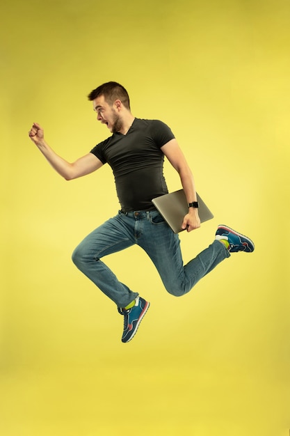 Foto grátis retrato de um homem feliz pulando com dispositivos isolados em amarelo