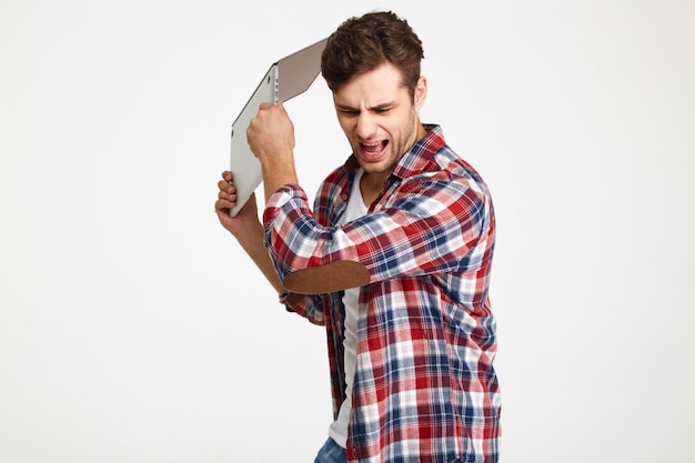 Retrato de um homem furioso irritado jogando seu computador portátil