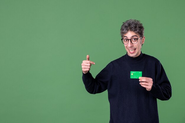 Retrato de um homem gênio segurando um cartão de crédito verde em estúdio tiro parede verde