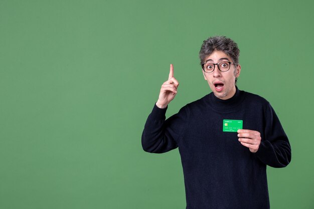 Retrato de um homem gênio segurando um cartão de crédito verde em estúdio tiro parede verde