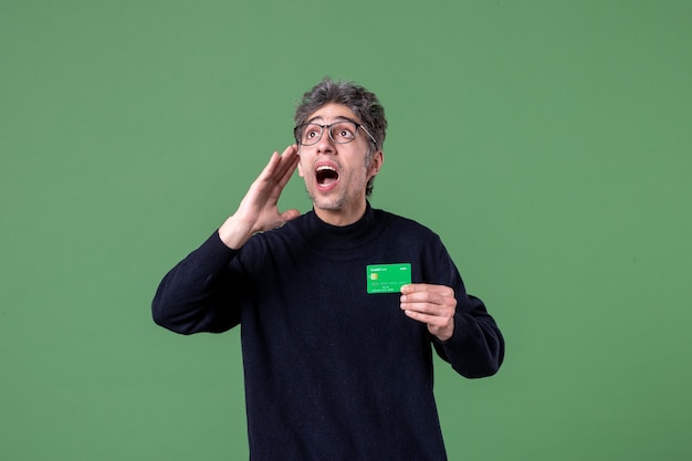 Retrato de um homem gênio segurando um cartão de crédito verde na parede verde