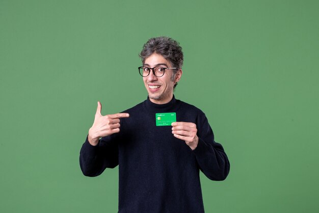 Retrato de um homem gênio segurando um cartão de crédito verde na parede verde