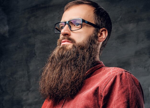 Retrato de um homem hipster barbudo em óculos vestido com uma camisa vermelha sobre fundo cinza.