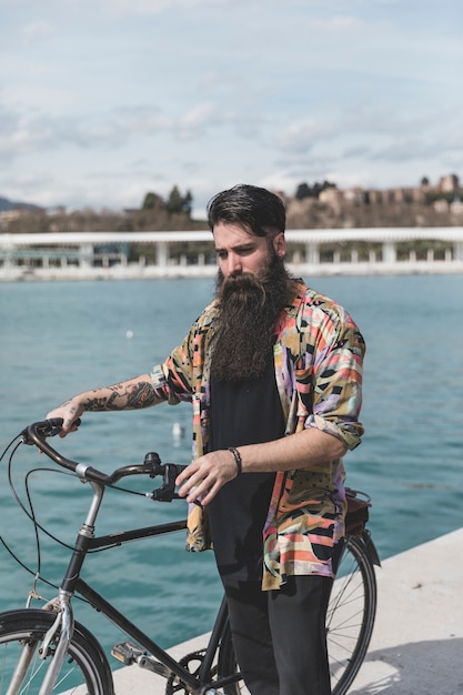 Foto grátis retrato, de, um, homem jovem, ficar, com, bicicleta, perto, a, costa