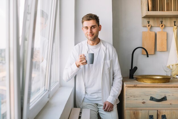 Retrato, de, um, homem jovem, segurando, xícara café, ficar, em, cozinha