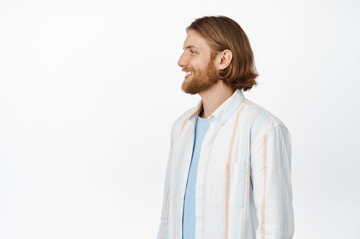 Foto grátis retrato de um homem loiro bonito com barba, olhando para a esquerda e sorrindo satisfeito, vestindo roupas casuais com uma expressão facial relaxada e feliz em branco
