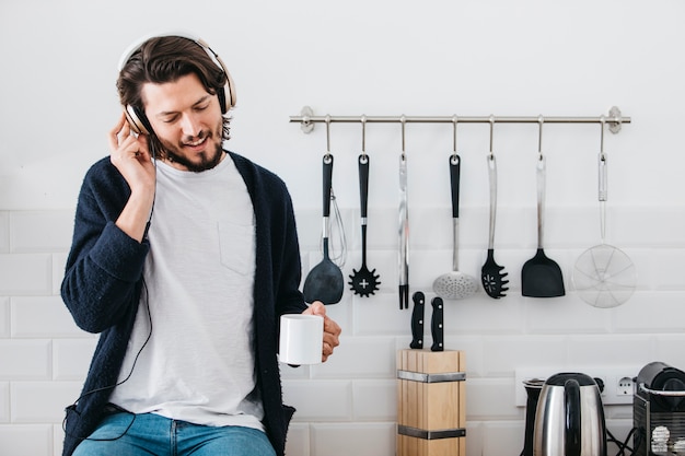 Foto grátis retrato de um homem ouvindo música no fone de ouvido sentado no balcão da cozinha