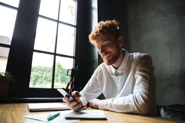 Retrato de um homem ruivo sorridente usando telefone celular