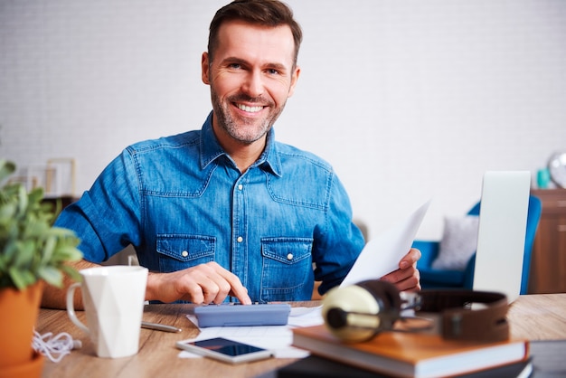 Retrato de um homem sorridente, calculando suas despesas mensais