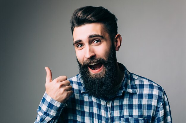 Retrato de um homem sorridente de óculos mostrando o polegar sobre uma parede cinza