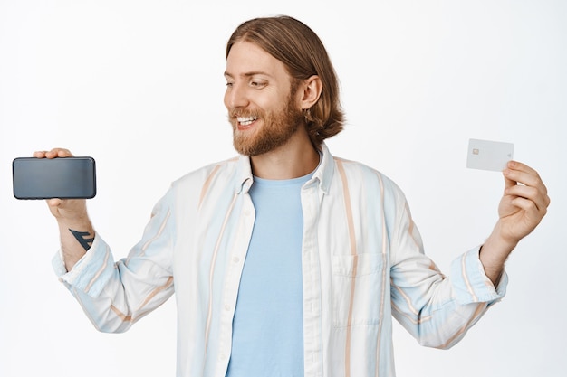 Retrato de um homem sorridente, mostrando a tela horizontal do smartphone e o cartão de crédito em branco