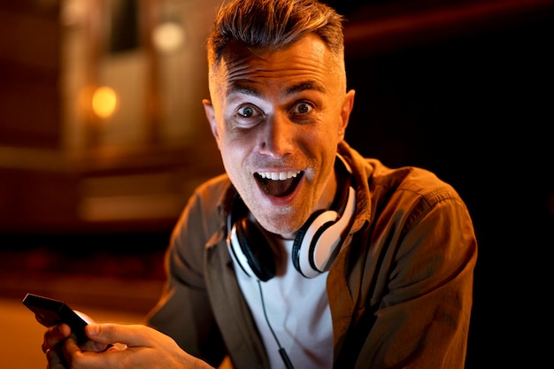 Retrato de um homem sorridente na cidade à noite com fones de ouvido e smartphone