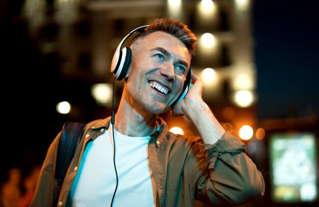 Retrato de um homem sorridente na cidade à noite com fones de ouvido