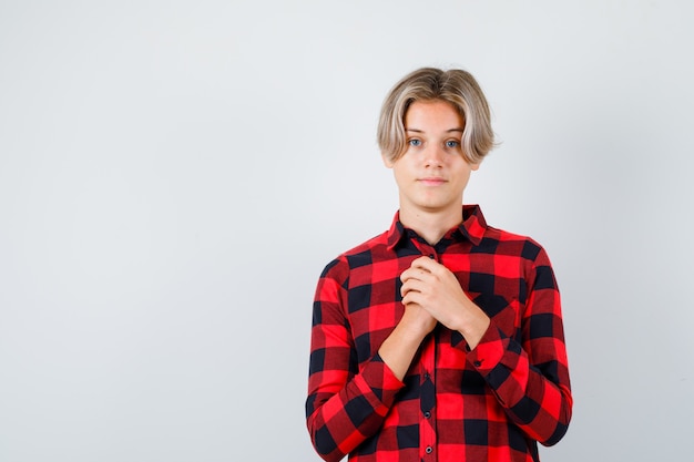 Retrato de um jovem adolescente com as mãos no peito em uma camisa quadrada e olhando esperançoso de frente
