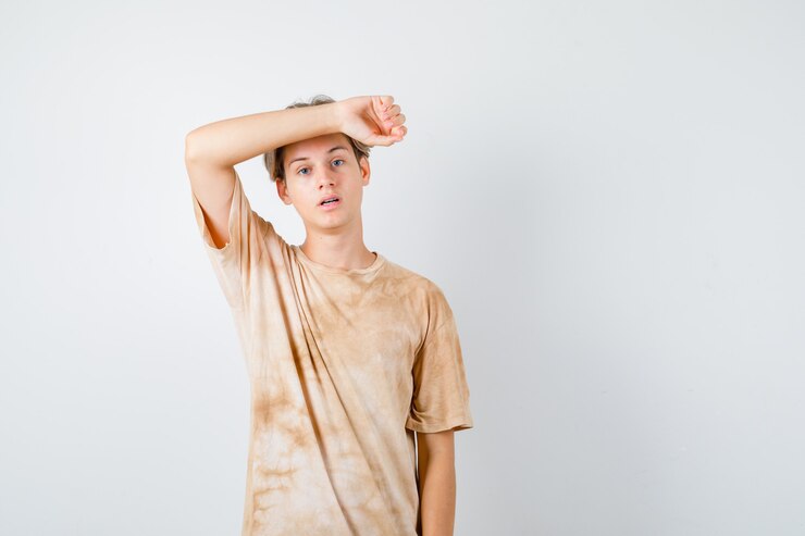 Foto grátis retrato de um jovem adolescente mantendo o braço na testa em uma camiseta e olhando melancolicamente a vista frontal