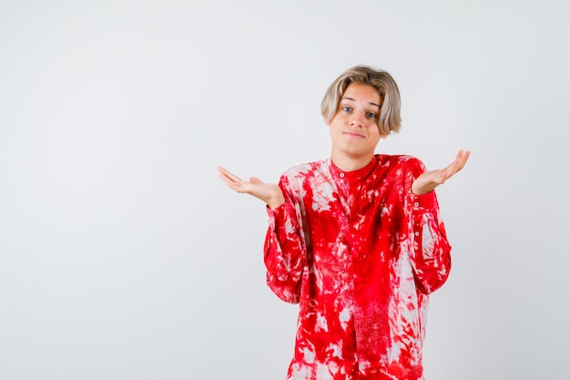 Retrato de um jovem adolescente mostrando um gesto de impotência na camisa e parecendo confuso com a vista frontal