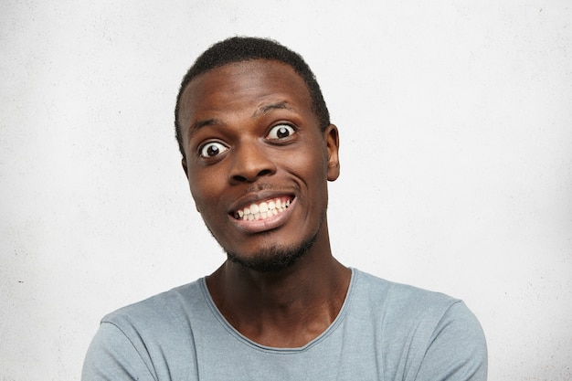 Retrato de um jovem africano engraçado e aterrorizado arregalando os olhos e mostrando os dentes