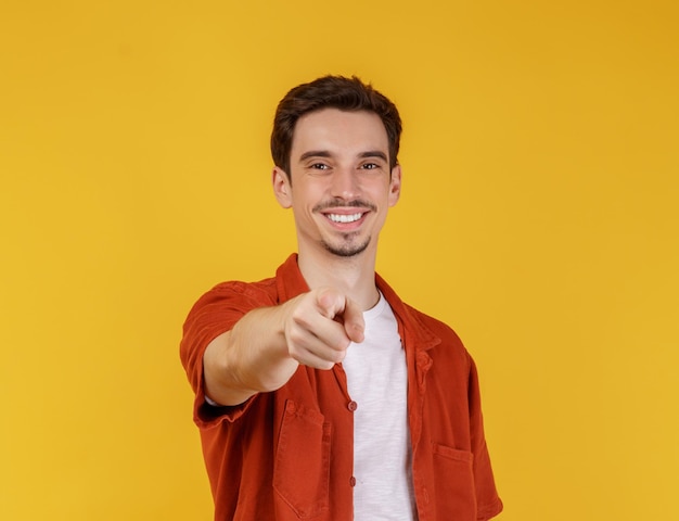 Retrato de um jovem atraente e alegre apontando o dedo para a câmera e de pé isolado sobre o fundo