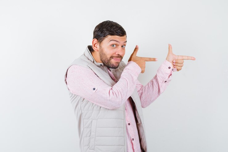 Foto grátis retrato de um jovem bonito apontando para a direita na camisa, colete e olhando de frente com curiosidade