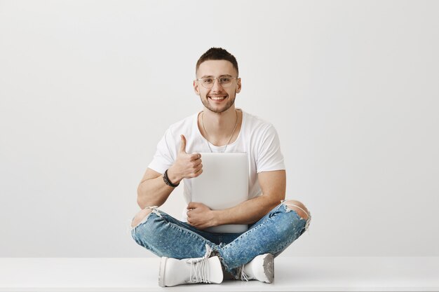 Retrato de um jovem bonito de óculos posando com seu laptop