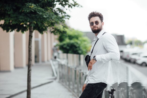 Retrato de um jovem bonito e elegante em uma camisa branca nas ruas da cidade em óculos de sol