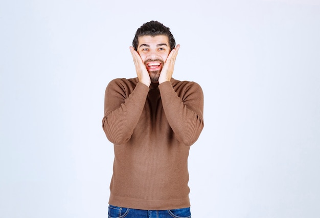 Retrato de um jovem bonito no suéter casual, segurando as palmas das mãos perto do rosto.