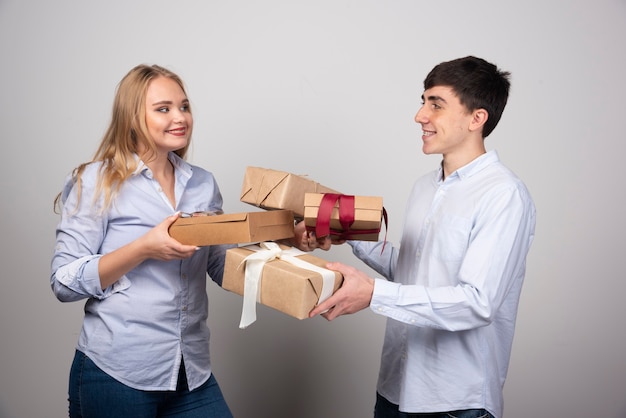 Retrato de um jovem casal alegre em pé e olhando um para o outro, segurando as caixas de presentes.
