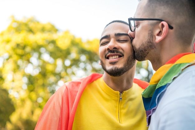 Foto grátis retrato de um jovem casal gay abraçando e mostrando seu amor com a bandeira do arco-íris no stret. lgbt e conceito de amor.